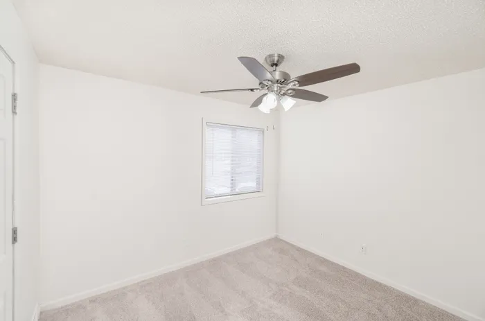 Bedroom with carpet, ceiling fan, window blinds, and neutral walls at Quail Ridge East Apartments.