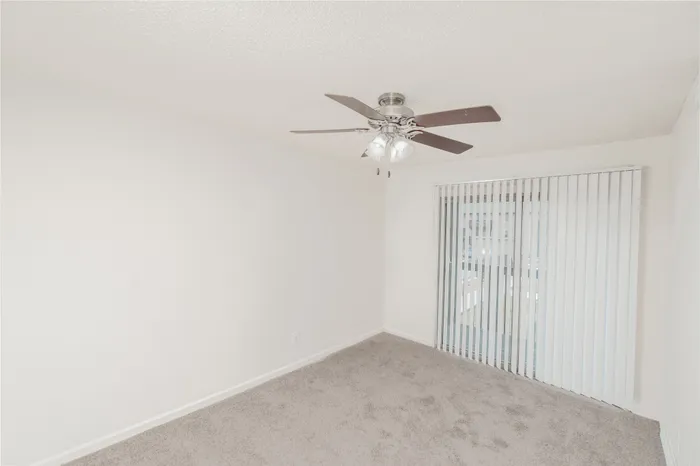 Bedroom with carpet, ceiling fan, closet space, and sliding glass door access at Quail Ridge East Apartments.