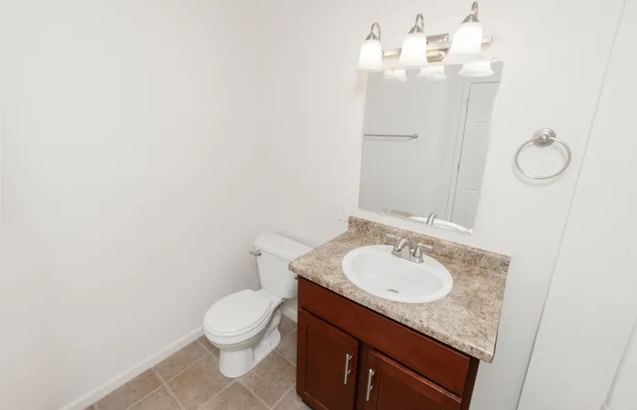 Bathroom with vanity storage, toilet, tile flooring, and updated lighting at Quail Ridge East Apartments.