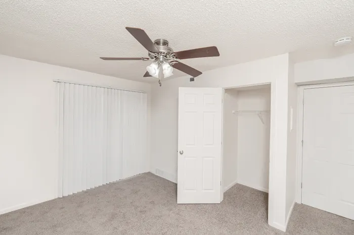 Bedroom with carpet, ceiling fan, window blinds, and closet at Quail Ridge East Apartments.