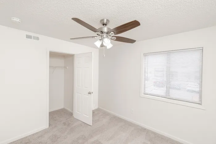 Bright bedroom with plush carpeting, large window, and ceiling fan, offering comfort and style.