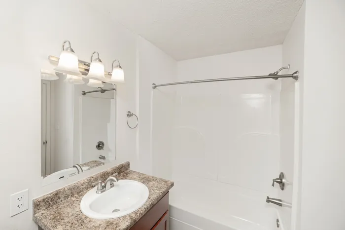 Bathroom with vanity, tub shower combo, modern lighting, and neutral finishes at Quail Ridge East Apartments.