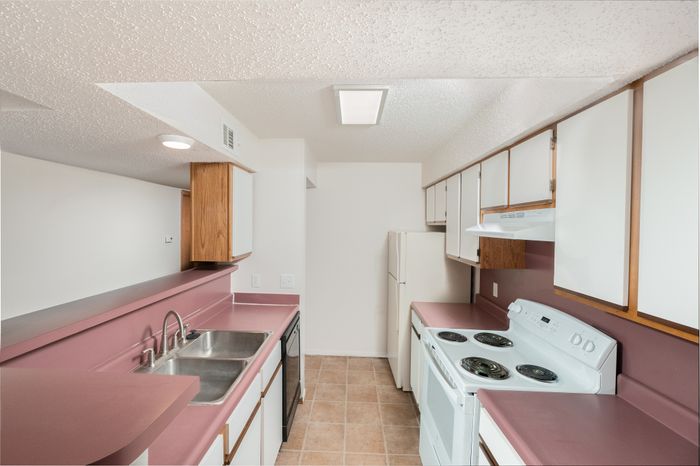 Kitchen with double sink, electric range, refrigerator, and laminate countertops with wood-trim cabinetry.