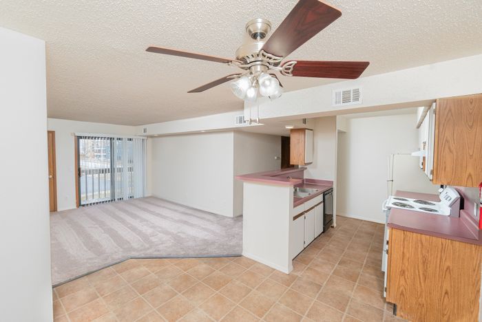 Open floor plan with kitchen breakfast bar, tile flooring, carpeted living room, ceiling fan, and sliding patio door.