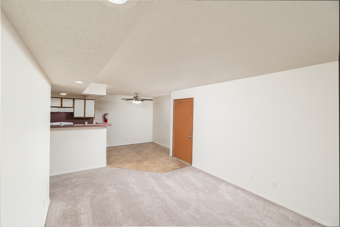 Spacious living room with beige carpet, ceiling fan, neutral walls, and open breakfast bar leading to kitchen.
