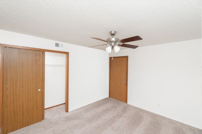 Bedroom with beige carpet, ceiling fan, window, and sliding closet doors.