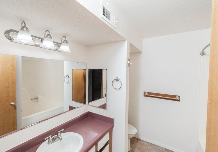 Bathroom vanity with laminate countertop, mirror, lighting fixture, tub, and toilet area.