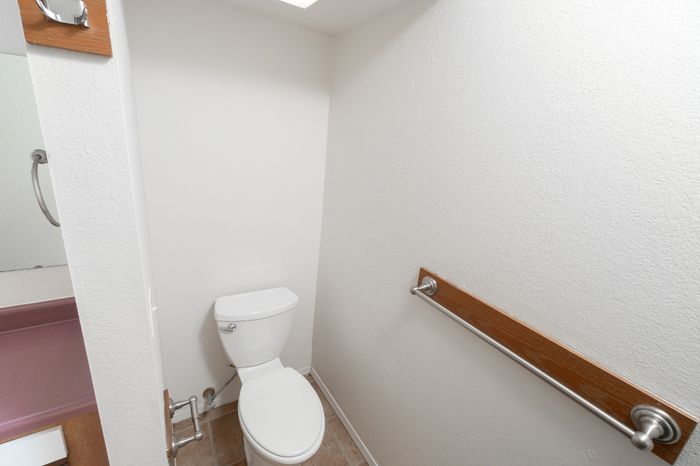 Bathroom toilet area with towel bar, tile floor, and adjacent vanity space.