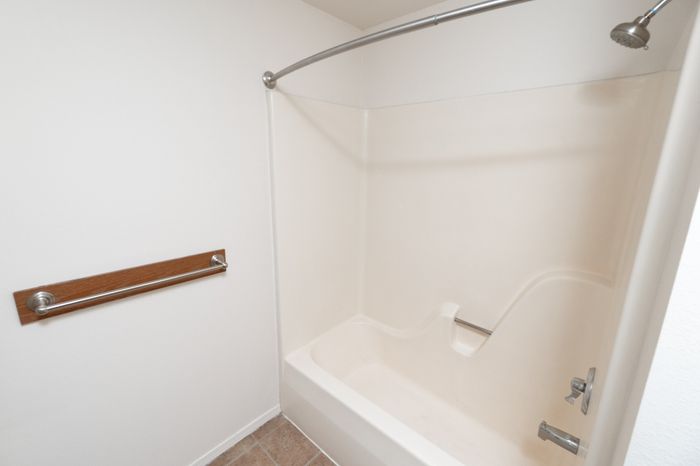 Bathroom with tub-shower combo, curved curtain rod, tile flooring, and grab bar.