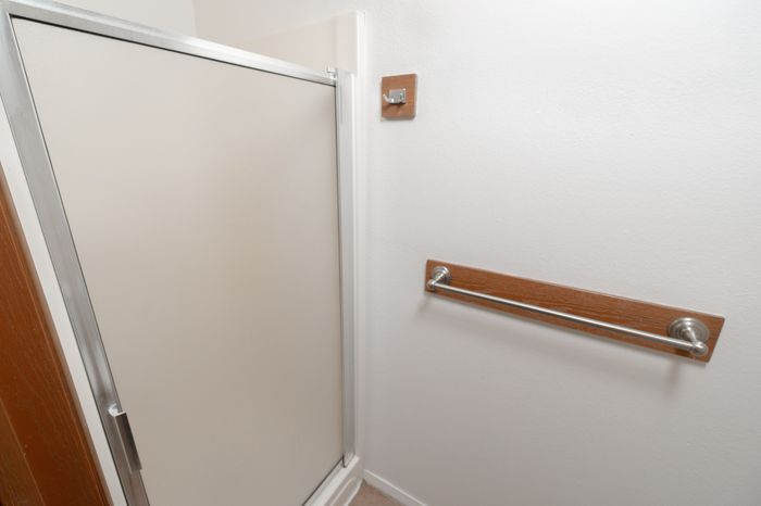 Bathroom shower with frosted glass door, towel bar, and tile flooring.