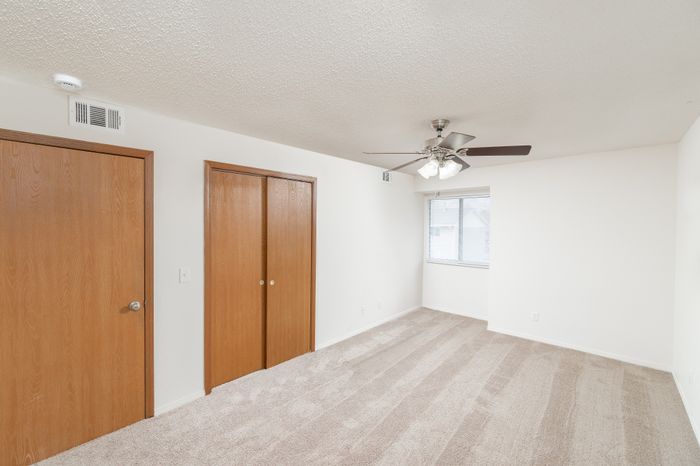 Bedroom with beige carpet, ceiling fan, window, and sliding closet doors.