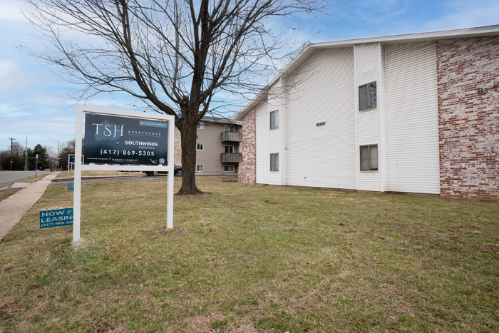 TSH Apartments exterior with monument sign, lawn, mature tree, and brick and siding apartment buildings along South Avenue.