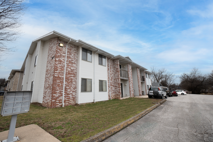 TSH Apartments exterior building with brick and siding facade, balconies, parking area, and community mailbox.