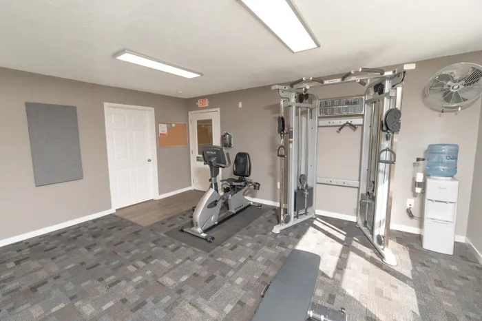 Apartment fitness center featuring cable weight machine, recumbent bike, workout bench, and water station.