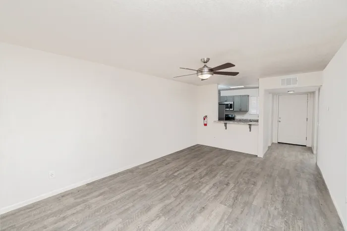 Open living room at Hillcrest 90 Apartments with wood-style flooring, ceiling fan, neutral walls, and breakfast bar overlooking the kitchen.