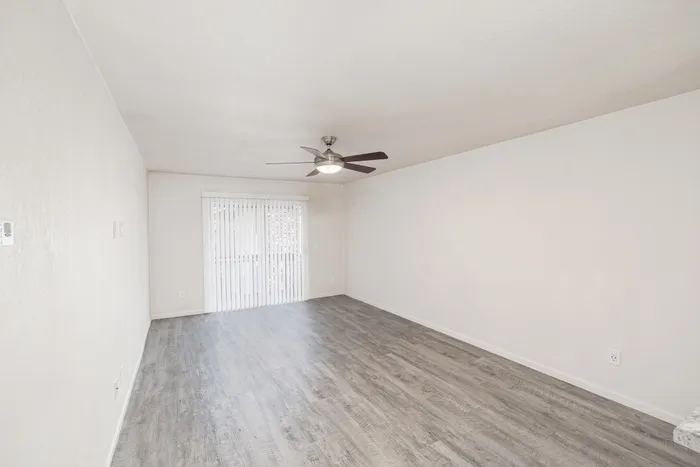 Spacious Hillcrest 90 living area with wood-look flooring, ceiling fan, neutral walls, and sliding glass doors leading to a private patio or balcony.