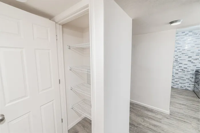 Hillcrest 90 apartment entry hallway with pantry storage shelves, wood-style flooring, and view toward the updated kitchen area.