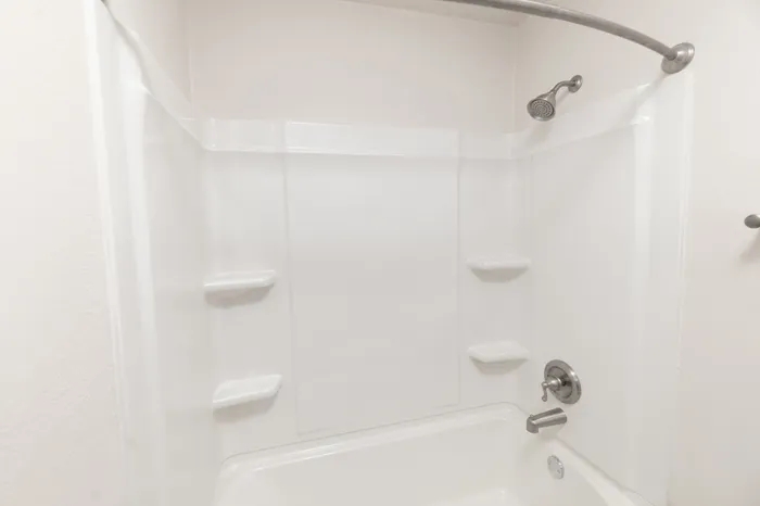 Hillcrest 90 bathroom featuring a white tub and shower combination with built-in shelves, curved curtain rod, and brushed nickel fixtures.