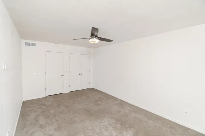 Spacious Hillcrest 90 bedroom with plush carpet, ceiling fan with light, neutral walls, and window with blinds for natural light.