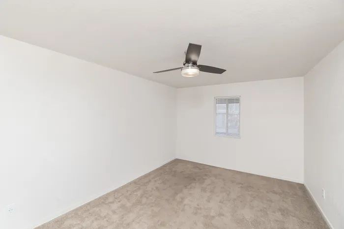 Spacious Hillcrest 90 bedroom with plush carpet, ceiling fan with light, neutral walls, and window with blinds for natural light.