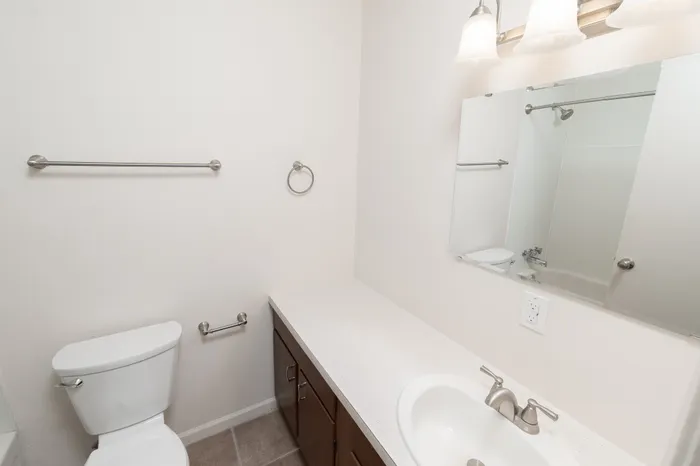 Hillcrest 90 bathroom with single sink vanity, large mirror with lighting, toilet, and tub shower combination visible in reflection.