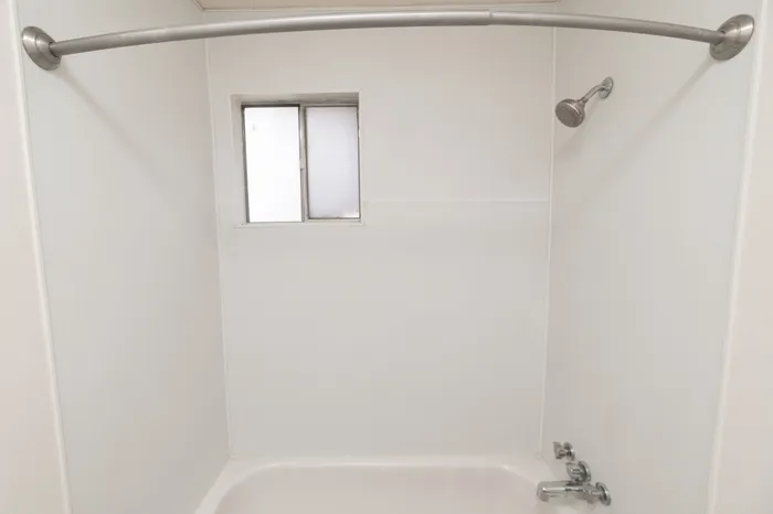 Bathroom tub and shower combination with curved curtain rod, wall surround panels, and small frosted window for natural light.