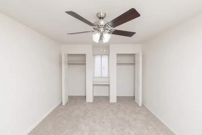 Bedroom with plush carpet, ceiling fan, recessed window ledge, and two closets with white double doors for storage.