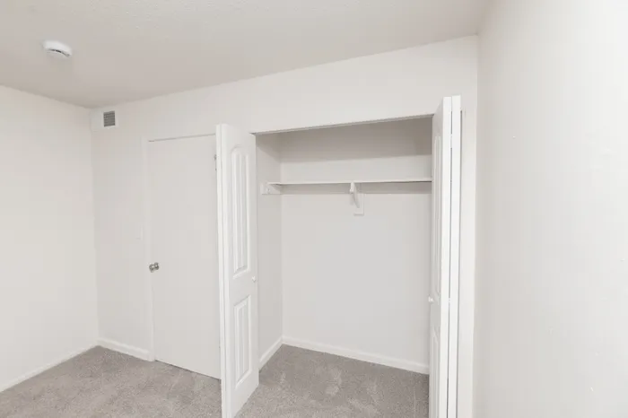 Spacious bedroom with carpet, ceiling fan with light, white closet doors, and entry door along the wall.