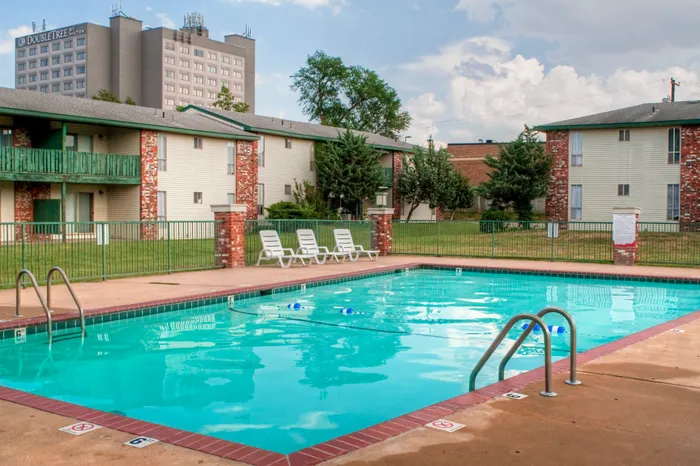 Inviting apartment complex with a sparkling swimming pool and lush green surroundings, perfect for relaxation and leisure.