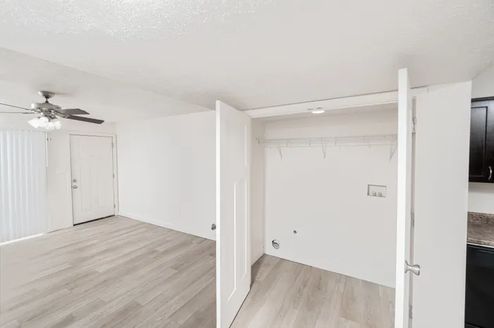 Laundry closet with washer and dryer hookups, wire shelving for storage, and double doors located near the living room area.