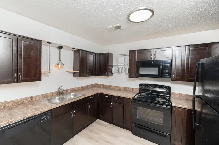 Spacious kitchen featuring dark wood cabinetry, laminate countertops, black electric stove, microwave, refrigerator, dishwasher, double-basin sink, and pendant lighting above the counter.