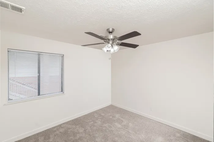 Bedroom with light carpet, white walls, ceiling fan with light, and window with blinds providing natural light.