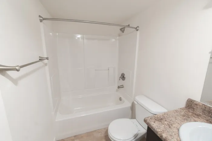 Full bathroom with white tub and shower combination, curved shower rod, toilet, towel bars, and laminate vanity countertop.