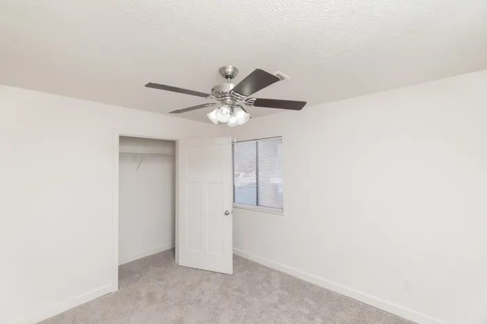 Bedroom featuring soft carpet flooring, ceiling fan with light, window with blinds, and open closet with built-in hanging rod.
