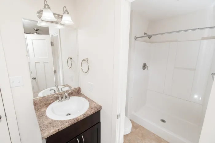 Bathroom with laminate vanity countertop, sink, mirror with overhead lighting, and walk-in shower with white surround.