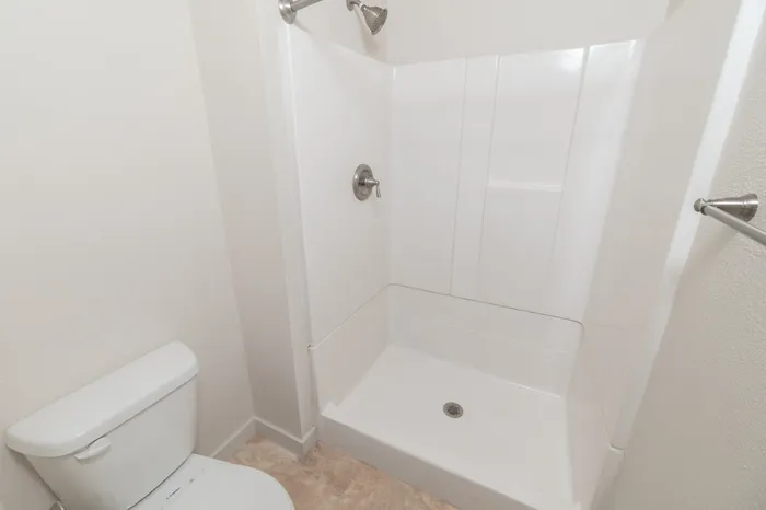 Bathroom featuring walk-in shower with white surround, toilet, and brushed nickel fixtures.