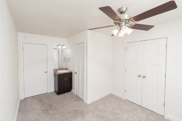 Bedroom with soft carpet, ceiling fan with light, built-in vanity sink with laminate countertop, and door leading to ensuite bathroom.
