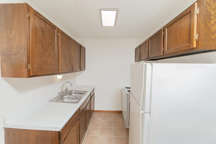 Kitchen with wood cabinetry, double sink, laminate countertops, white refrigerator and stove, and overhead lighting.