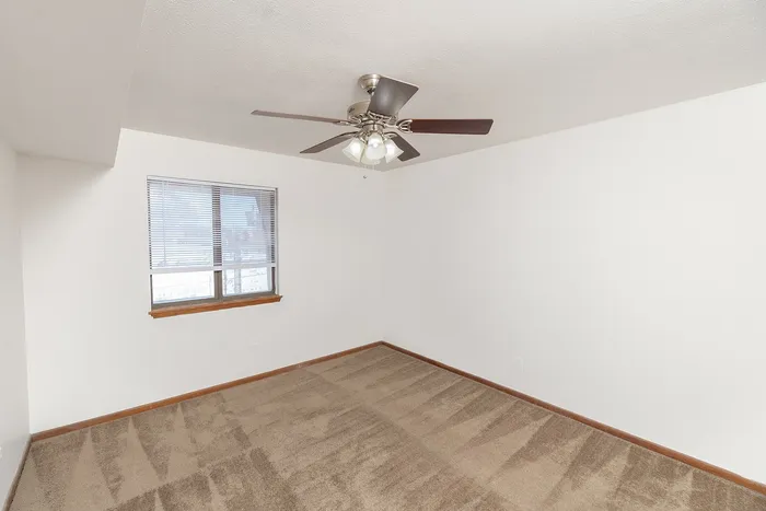 Bedroom with beige carpet, white walls, ceiling fan with light, and window with blinds for natural light.