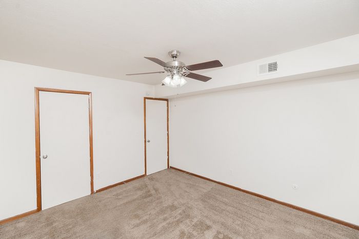 Bedroom with carpet flooring, ceiling fan, and two interior doors for closet and entry access.