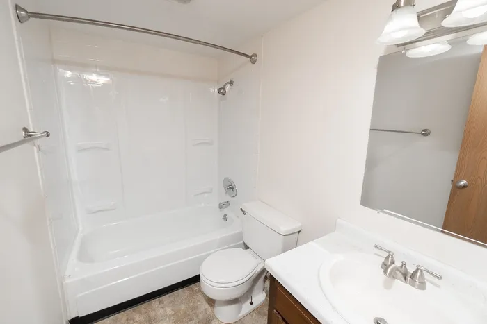Bathroom with tub and shower combo, white surround, vanity with sink, mirror lighting, and wood cabinetry.