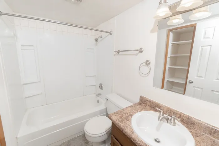 Full bathroom with tub and shower combo, white surround, vanity with sink and storage, mirror lighting, and built-in shelving.