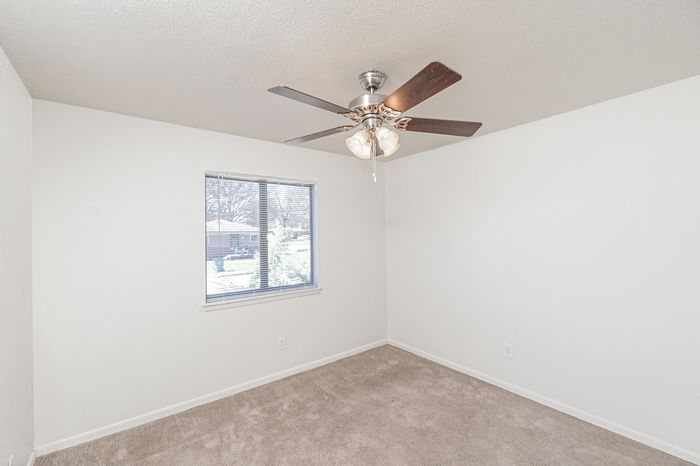 Bedroom with beige carpet, white walls, ceiling fan with light, and window with blinds providing natural light.
