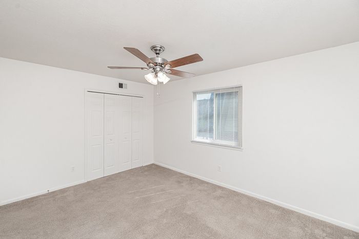 Bedroom featuring large closet with double doors, ceiling fan with light, and window bringing in natural light.