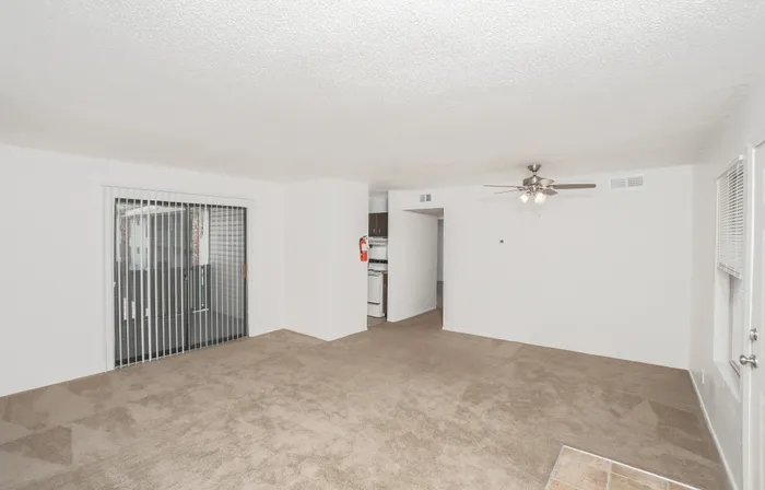Open living area with carpet flooring, ceiling fan, large window, and view into kitchen and hallway
