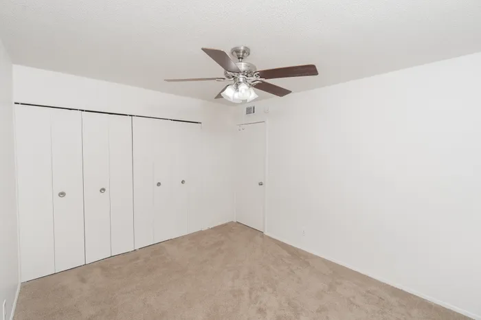 Bedroom featuring full length closet with sliding doors, ceiling fan with light, and soft carpet flooring
