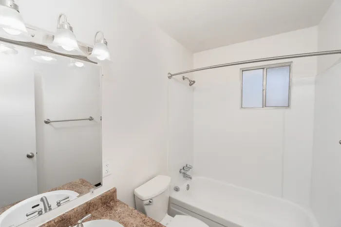 Bathroom with tub and shower combo, vanity with sink, mirror with lighting, and window for natural light