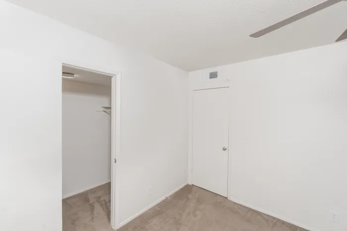 Bedroom with beige carpet, ceiling fan, window with blinds, and walk in closet entry with shelving