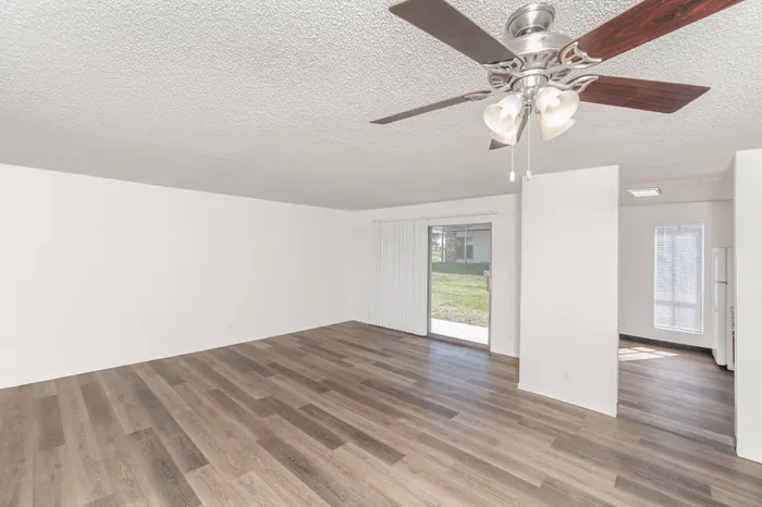 Open living area with wood style flooring, ceiling fan, and view into kitchen with natural light throughout