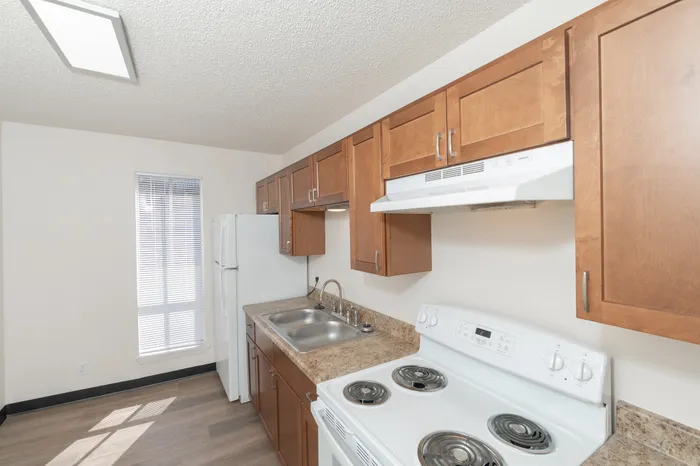 Updated kitchen with wood cabinets, laminate countertops, double sink, electric stove, and white appliances with natural light